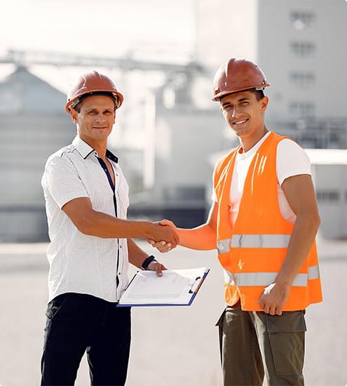 Two construction professionals shaking hands at a building site, symbolizing collaboration and trust in the construction industry