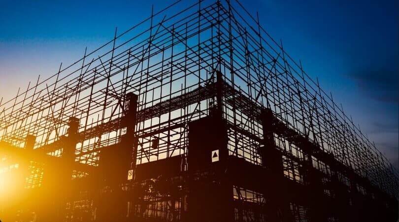 Silhouette of a building under construction with scaffolding at sunset