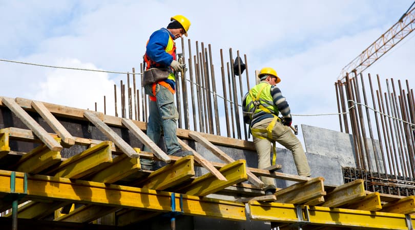 Two construction workers on scaffolding wearing hard hats and safety harnesses