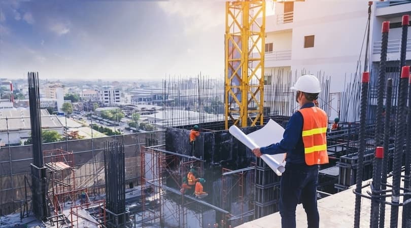 A construction site manager reviewing blueprints while looking over a building project