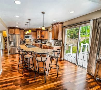 A spacious and well-lit kitchen with wooden cabinets, a central island with bar stools, stainless steel appliances, hardwood floors, and sliding glass doors leading to an outdoor area.